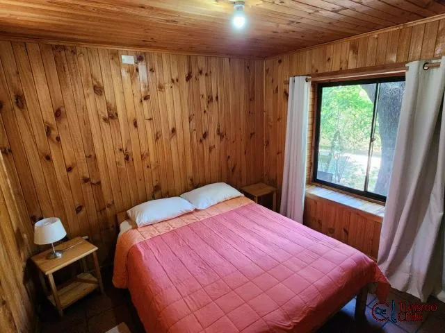 Dormitorio matrimonial con paredes de madera y ventana al jardín